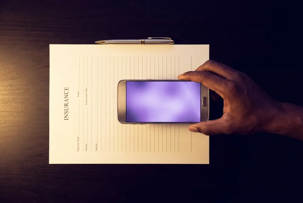 A hand photographing a document with a smartphone to upload it, the phone screen showing a soft glow